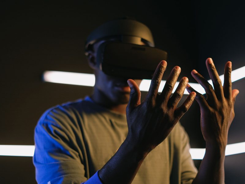 Man wearing a virtual reality headset with both hands raised to manipulate objects only he can see, lit by blue strip lighting