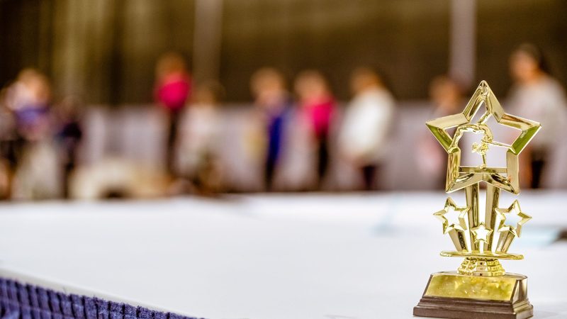 Gold star-shaped trophy standing on a draped table in the foreground while guests mingle out of focus behind it