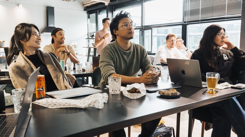 Young professionals gathered around a long table with open laptops, talking through a problem during a training workshop